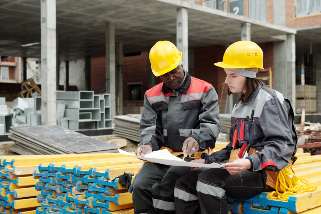 Mature black man and his young female colleague discussing blueprint