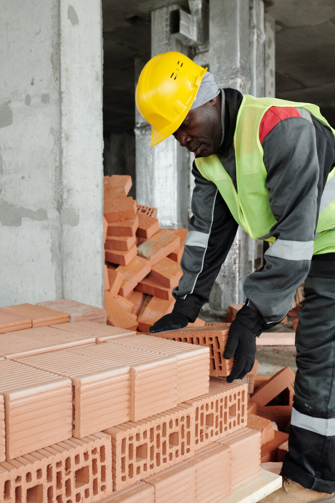 Mature experienced black man in workwear bending over stack of bricks