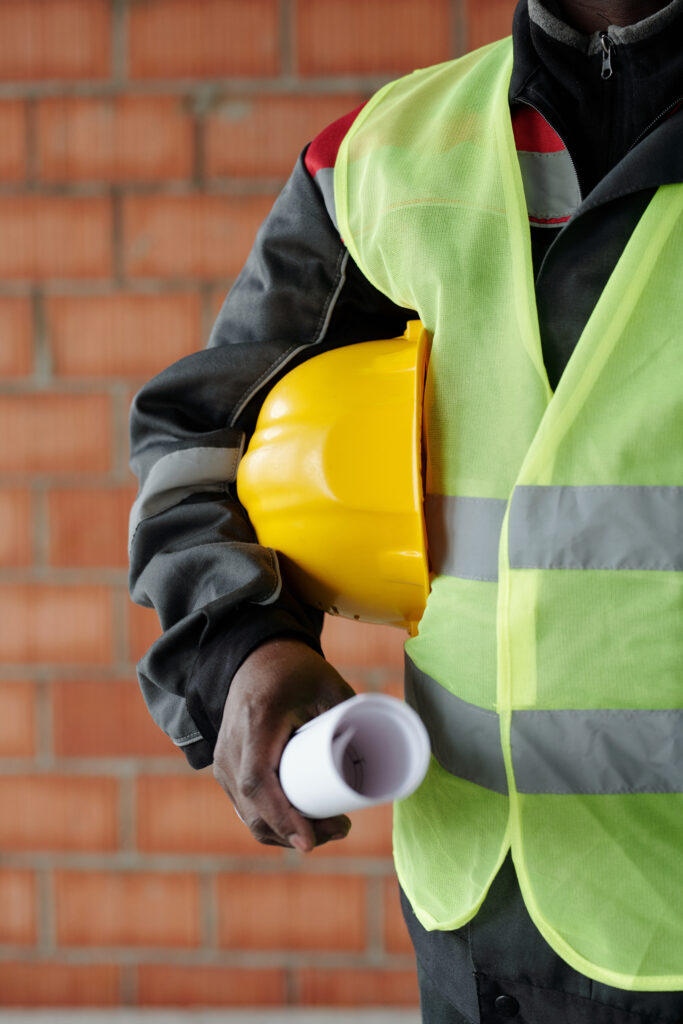 Part of modern foreman in reflective jacket holding hardhat and blueprint